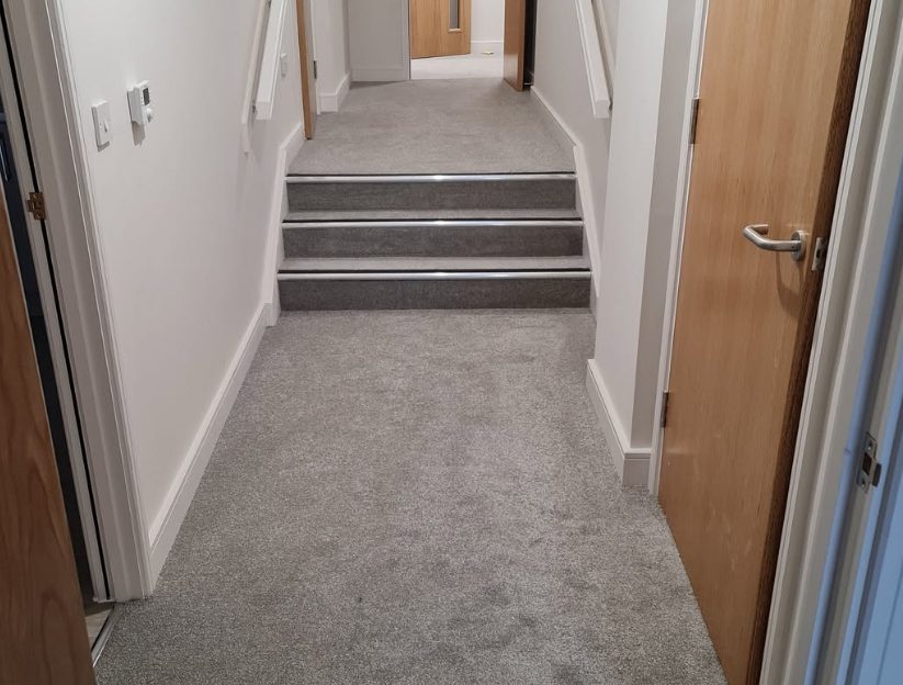 Grey carpet fitted across a hallway and short flight of stairs
