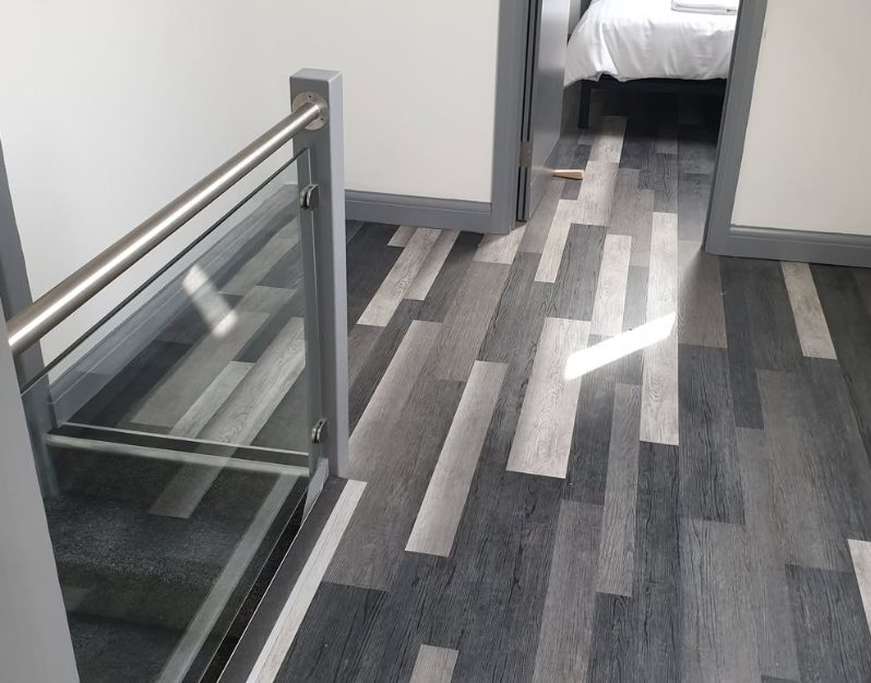 Grey plank-pattern flooring beside a glass balustrade and doorway