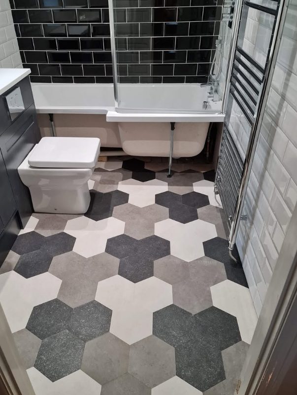 Hexagonal-pattern bathroom floor beside a bathtub and black wall tiles