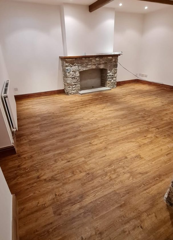 Wood plank flooring in a living room beside a stone fireplace