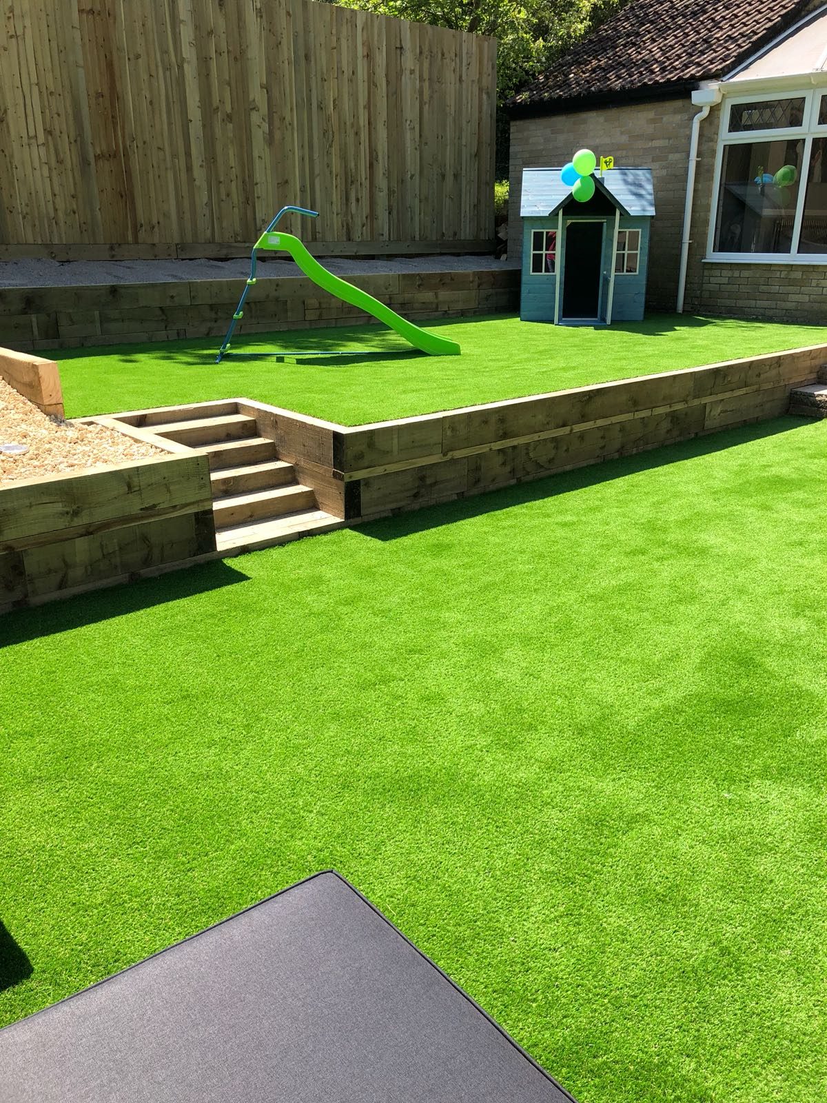 Artificial grass garden with timber steps and a children’s playhouse