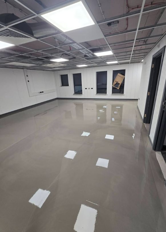 Smooth reflective subfloor in a commercial room with ceiling work underway