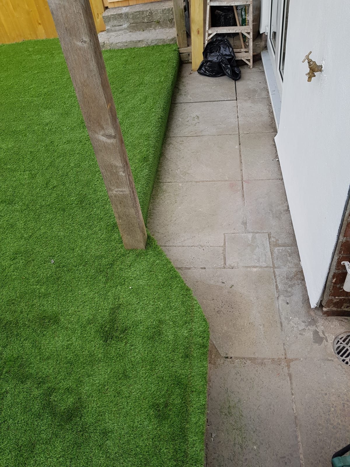 Artificial grass fitted beside a paved side path and house wall
