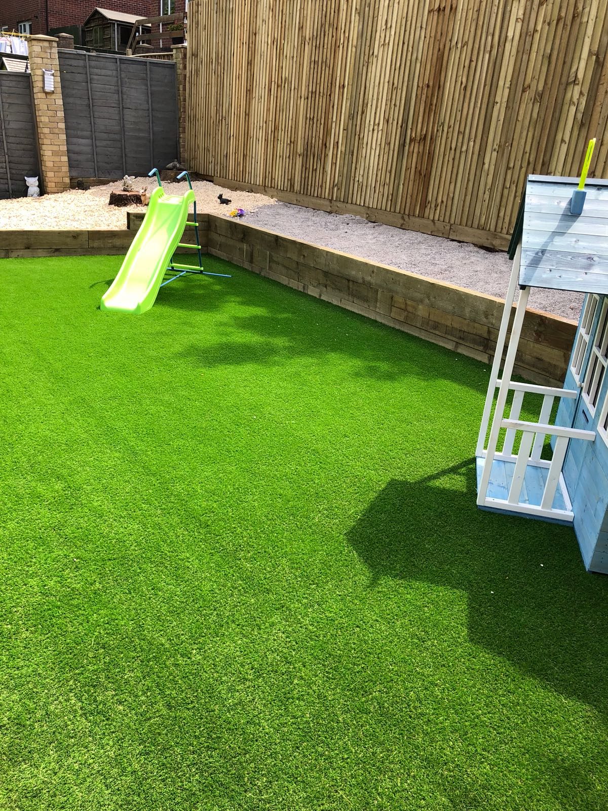 Artificial grass garden beside a children’s slide and timber fence