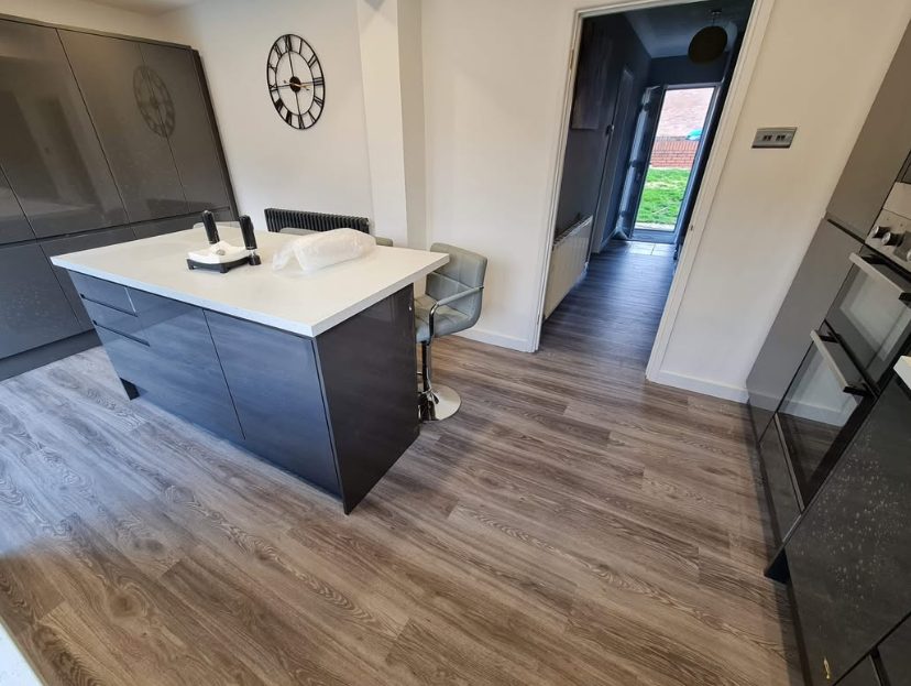 Wood-effect kitchen flooring around a dark island and fitted cabinets