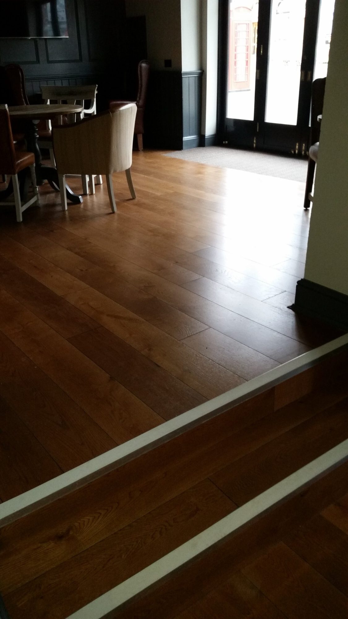 Dark wood-tone flooring beside an interior step and dining area