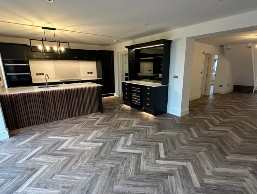 Grey wood-effect herringbone kitchen flooring around dark cabinets