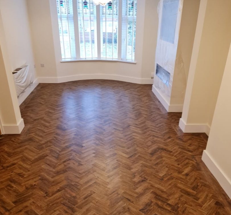 Rich wood-tone parquet herringbone floor beside a bay window and fireplace