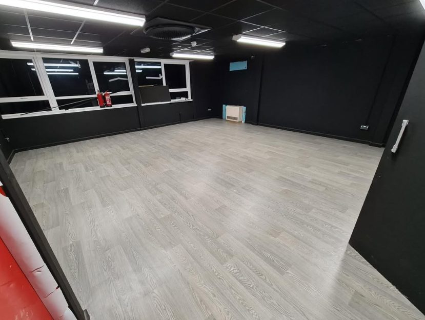 Light wood-effect commercial flooring in a dark-walled room
