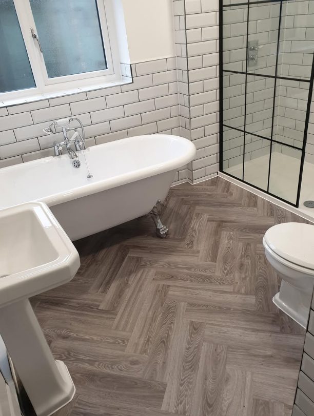Wood-effect herringbone bathroom floor beside a freestanding bath and shower
