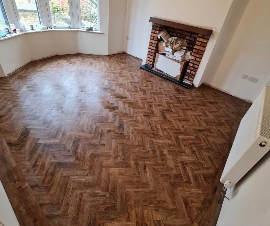 Dark herringbone flooring in a room with a bay window and brick fireplace