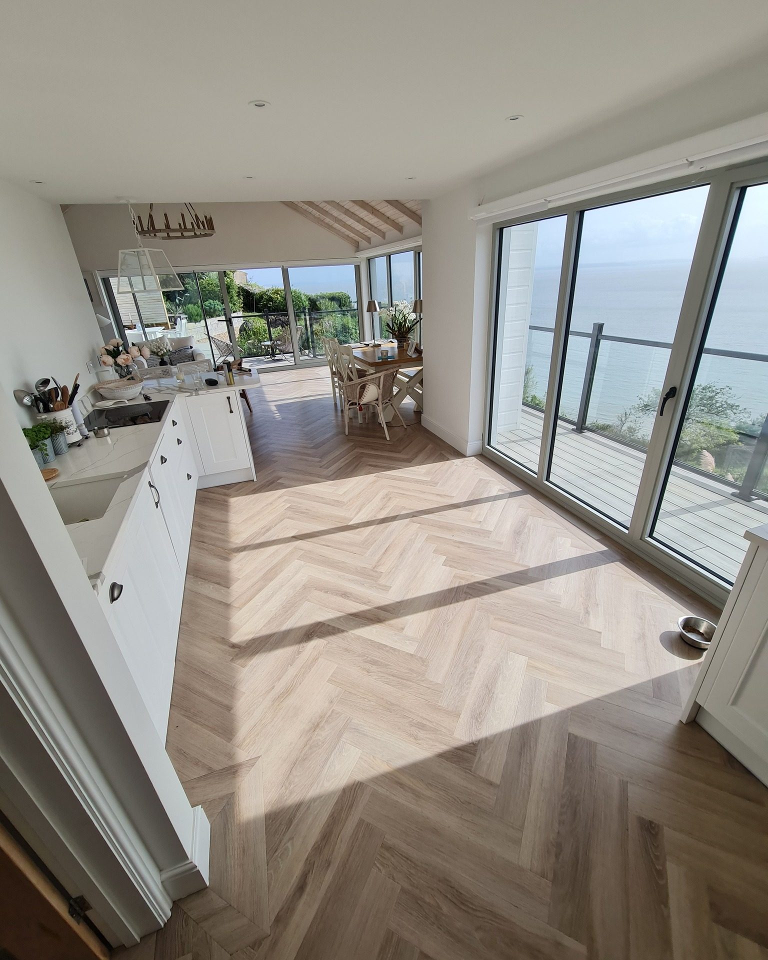 Pale herringbone-pattern flooring through an open-plan kitchen and dining space